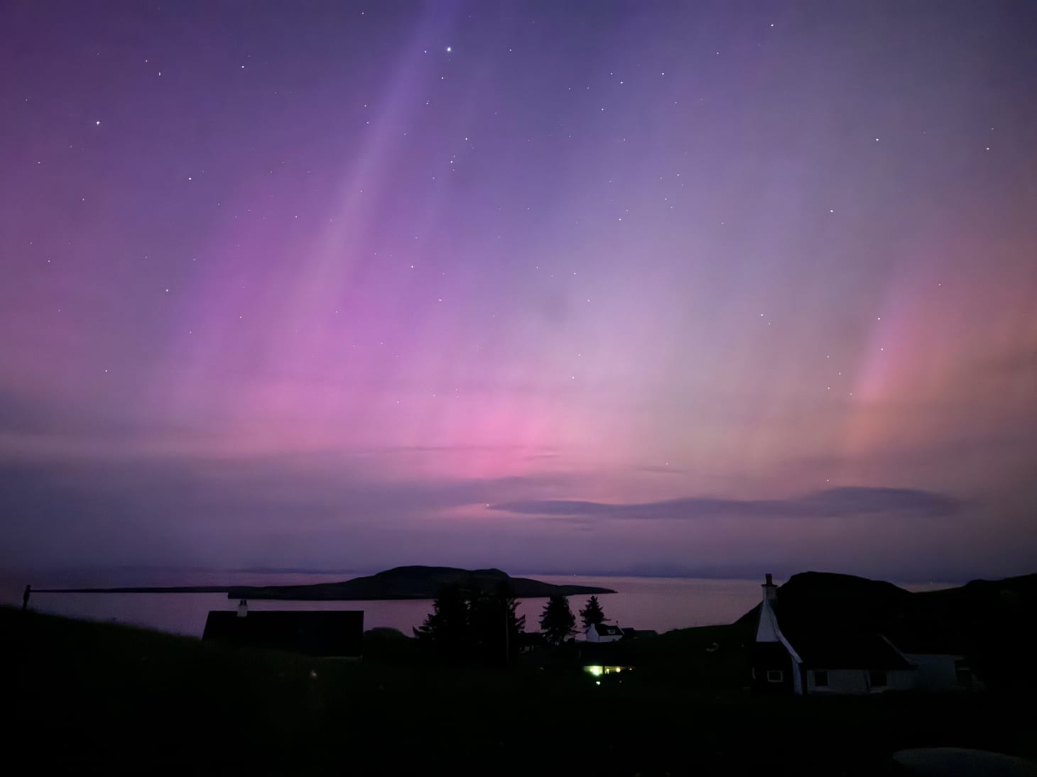 an island in the north minch under purple aurora lights from solar storm against star filled sky