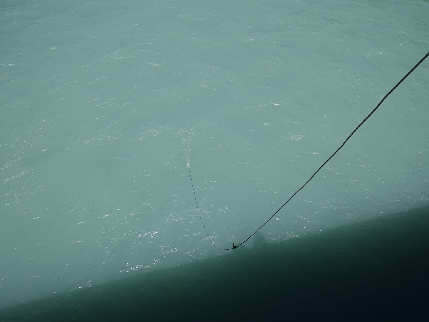 a curved line connected to a hydrophone dropping from a high place into blue river water